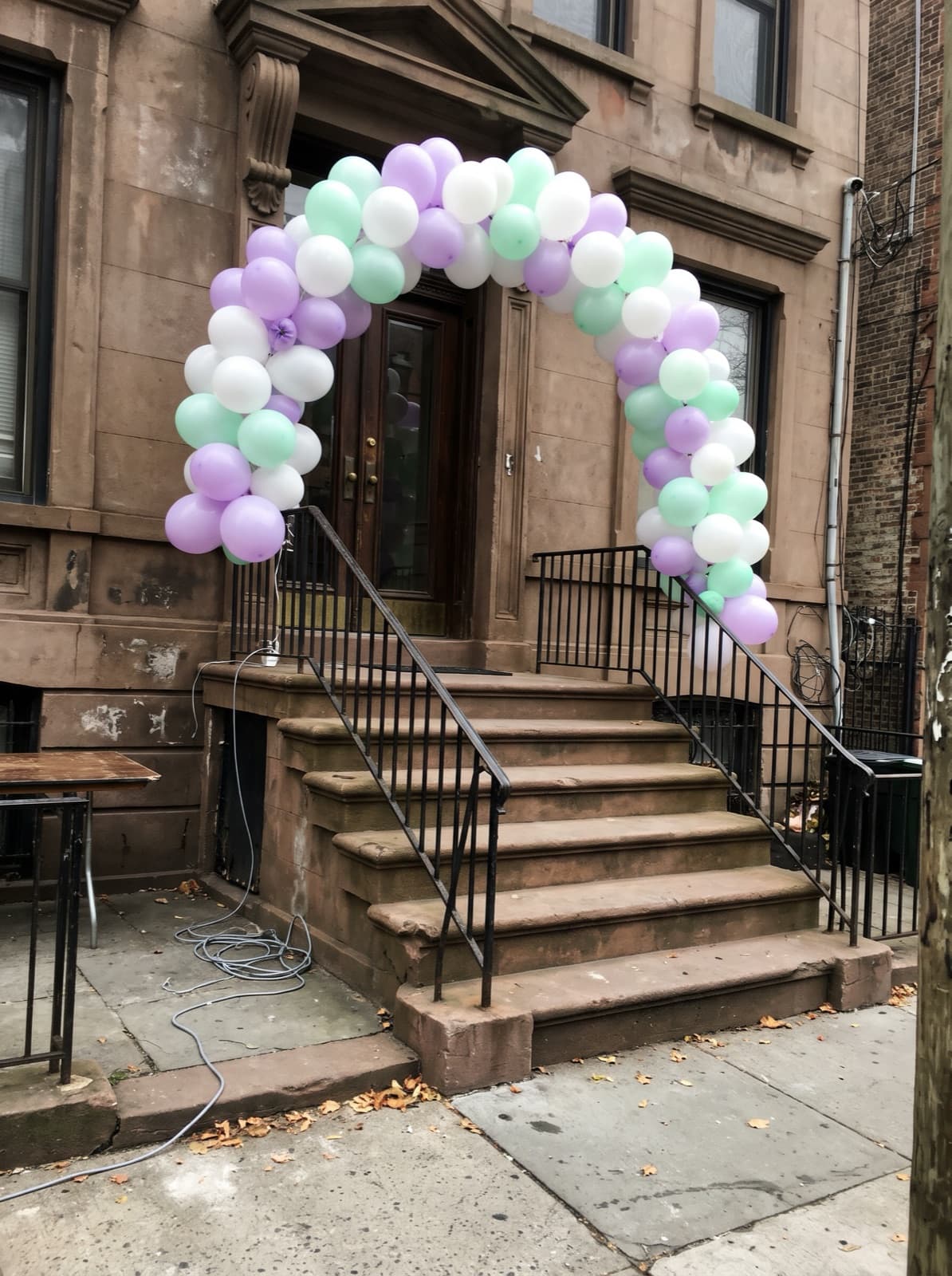 Balloon arch around a brownstone front door in lilac, mint and white